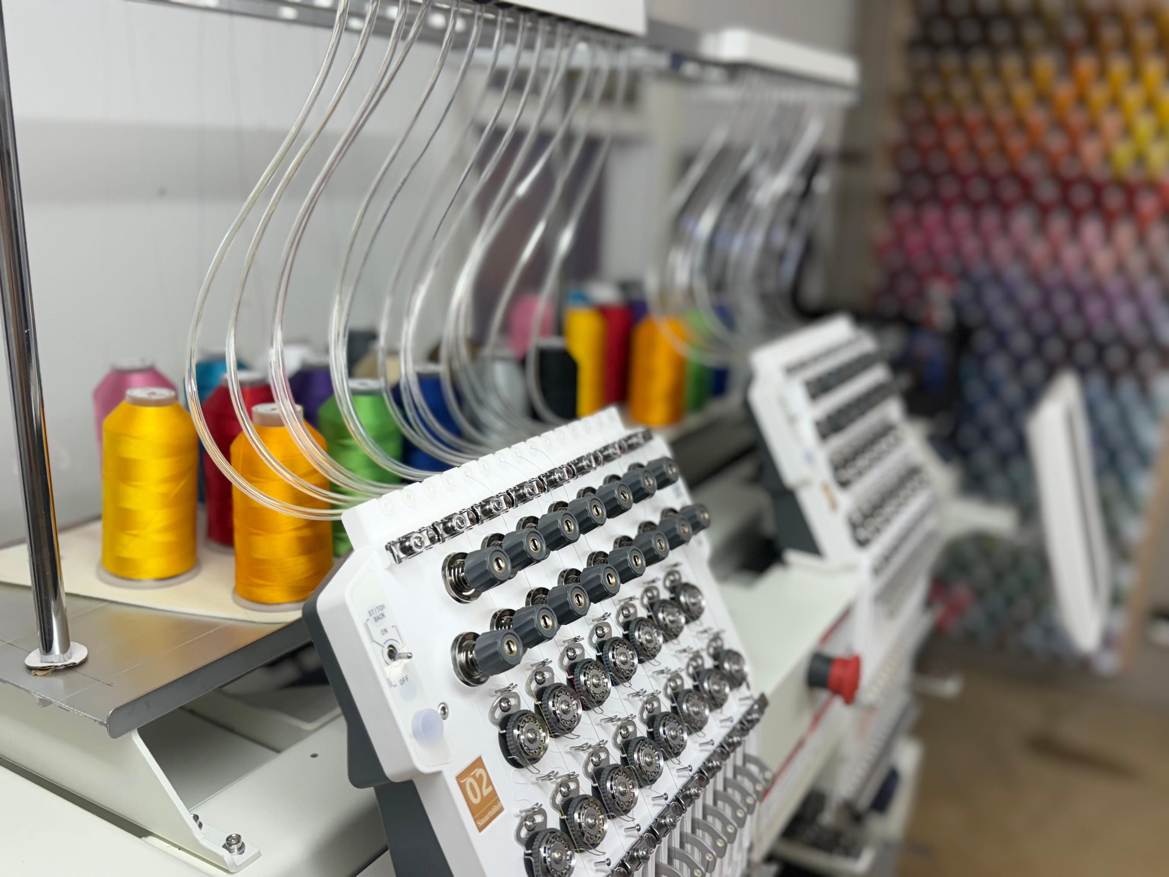 Embroidery machine setup with spools of colorful thread and translucent tubing, against a backdrop of a diverse thread color display.